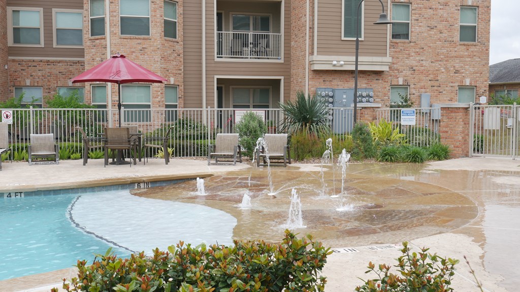 A pool with a fountain in front of a brick building.