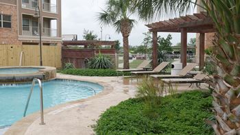 A pool surrounded by a concrete patio and a wooden pergola.