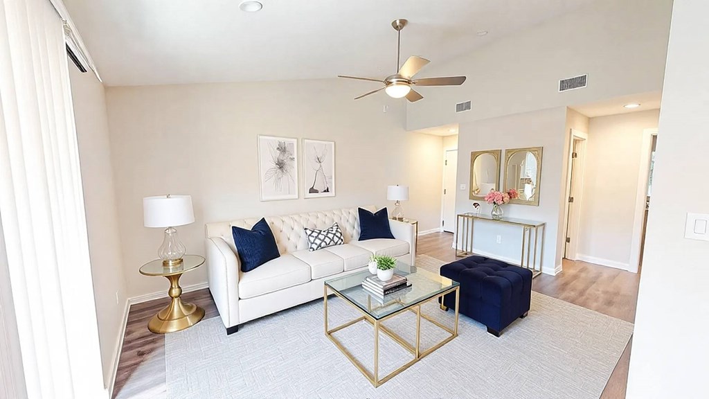 A living room with a white couch, a glass coffee table, and a ceiling fan.