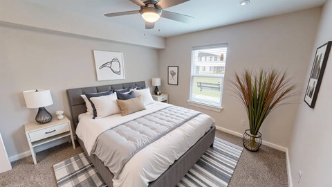 A bedroom with a bed, nightstand, and a plant.