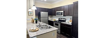 A kitchen with a refrigerator, microwave, oven, and sink.