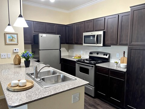 A kitchen with a refrigerator, microwave, oven, and sink.