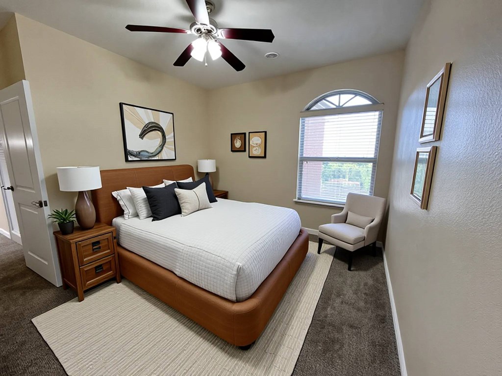 A bedroom with a large bed, a ceiling fan, and a window with blinds.