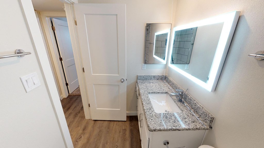 A bathroom with a granite counter top and a mirror with lights.