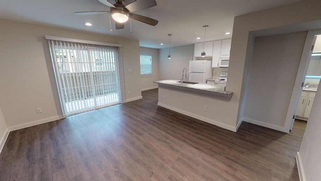 A spacious kitchen and living room with hardwood floors and a ceiling fan.