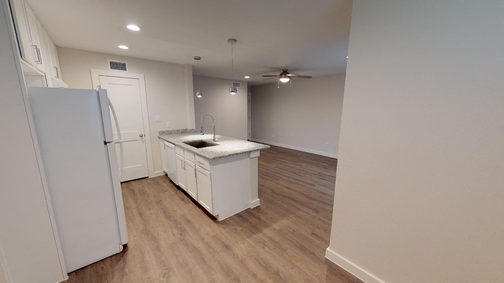 A white refrigerator stands in a kitchen with wooden floors and white walls.
