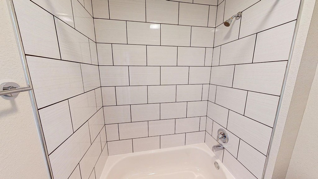 A white tiled shower with a white tub and a white door.
