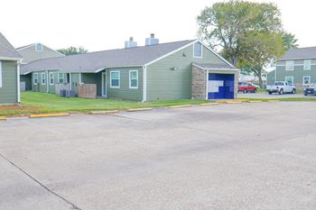 A parking lot in front of a green building with a blue garage door.