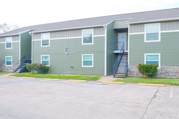 Apartment building with green siding and a parking lot in front.