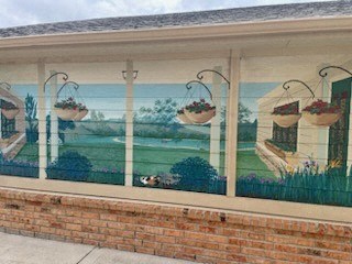 A mural on a wall depicts a serene garden scene with hanging baskets of fruit.
