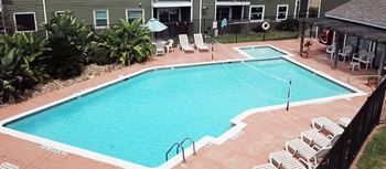 A rectangular pool surrounded by a concrete patio and a black fence.