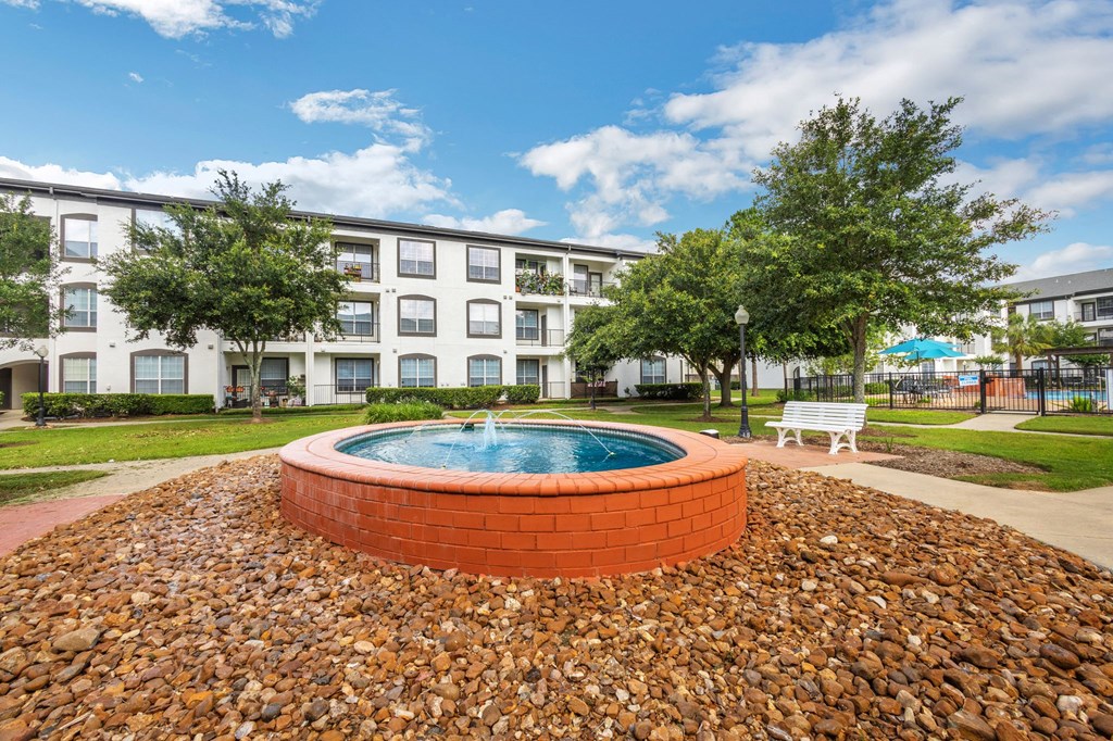 a round brick fountain sits in front of an apartment building