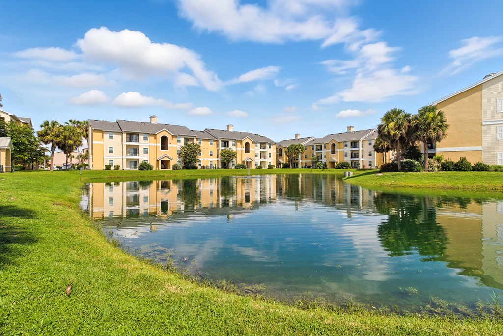 A pond in front of apartment buildings reflects the buildings and sky.