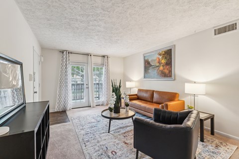 A living room with a brown leather couch, a black armchair, a coffee table, and a painting on the wall.
