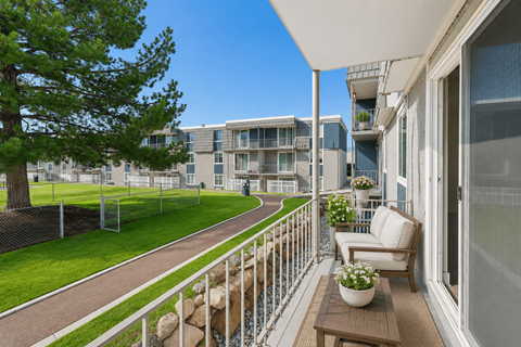 A balcony with a table and chairs overlooks a building and a tree.