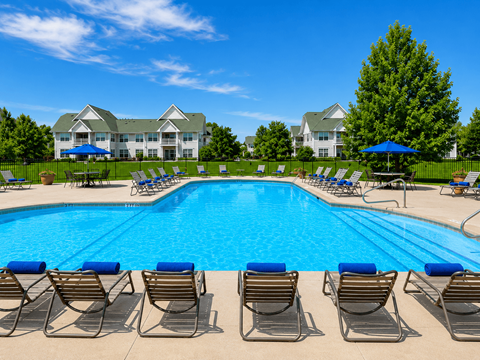 A swimming pool surrounded by lounge chairs and umbrellas with a building in the background.