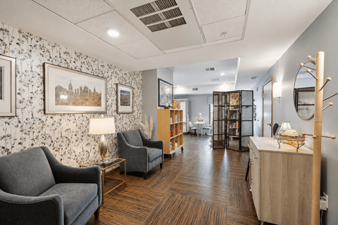 A waiting room with a grey sofa, a wooden table, and a wall with a floral pattern.