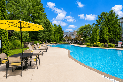 A pool with a yellow umbrella and chairs around it.