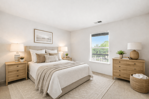 A well-lit bedroom with a large bed, two nightstands, and a window showing an outdoor view.