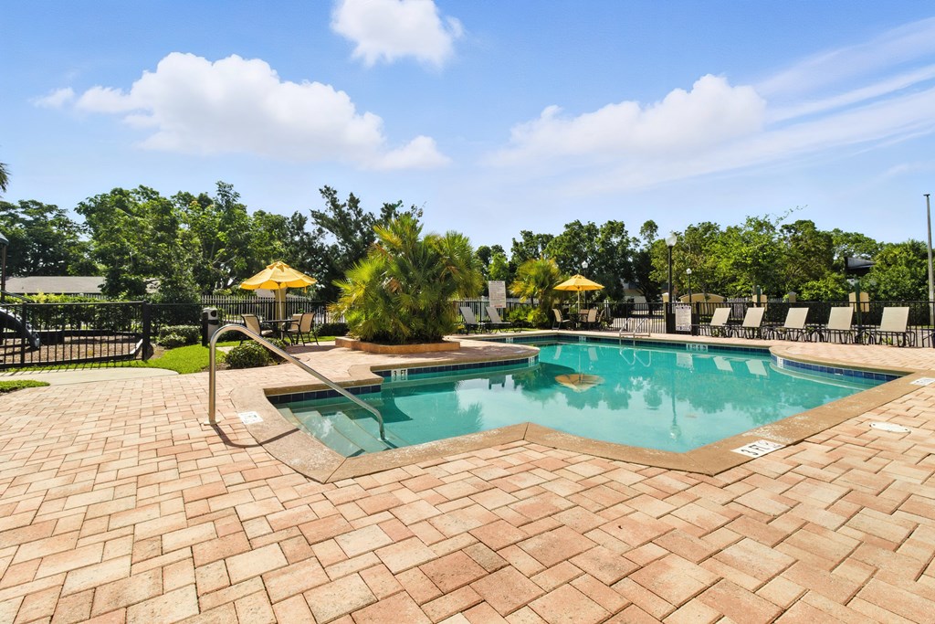 A pool surrounded by a brick patio and trees.