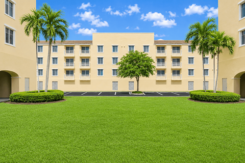 A large building with a green lawn in front and palm trees on the side.