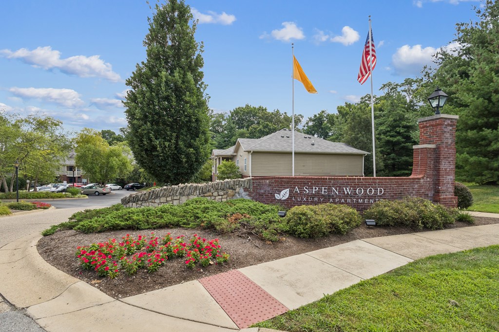 The image shows a well-maintained entrance to A Spenwood Apartments with a flagpole and a brick wall.