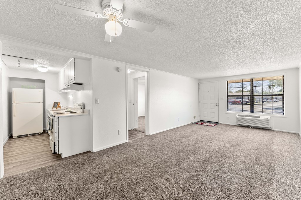 an empty living room with a kitchen and a ceiling fan