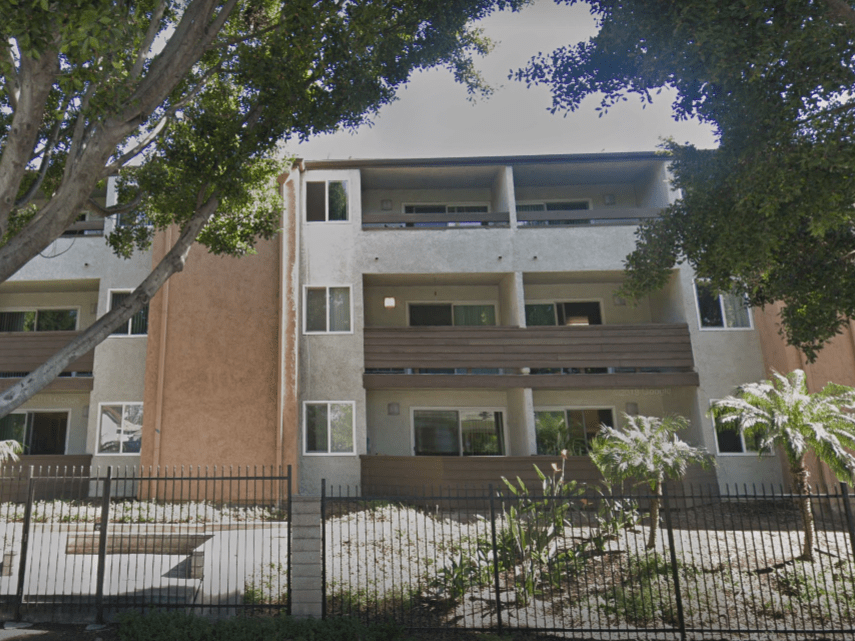an image of an apartment building with trees and a fence