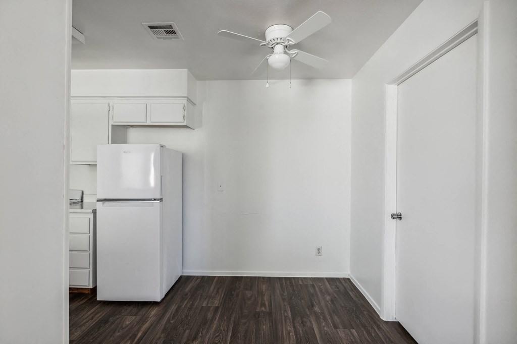 an empty room with a white refrigerator and a ceiling fan