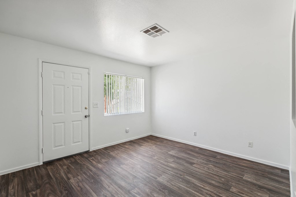 the living room of an apartment with white walls and wood floors