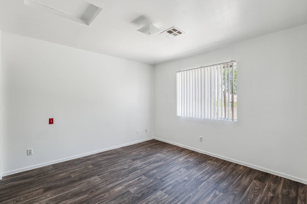 a bedroom with white walls and wood floors and a window