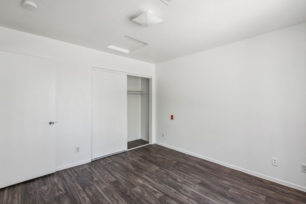 a bedroom with white walls and wood flooring and a closet
