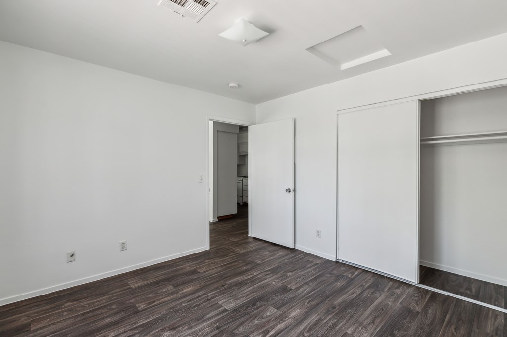 a bedroom with white walls and wood flooring and a closet