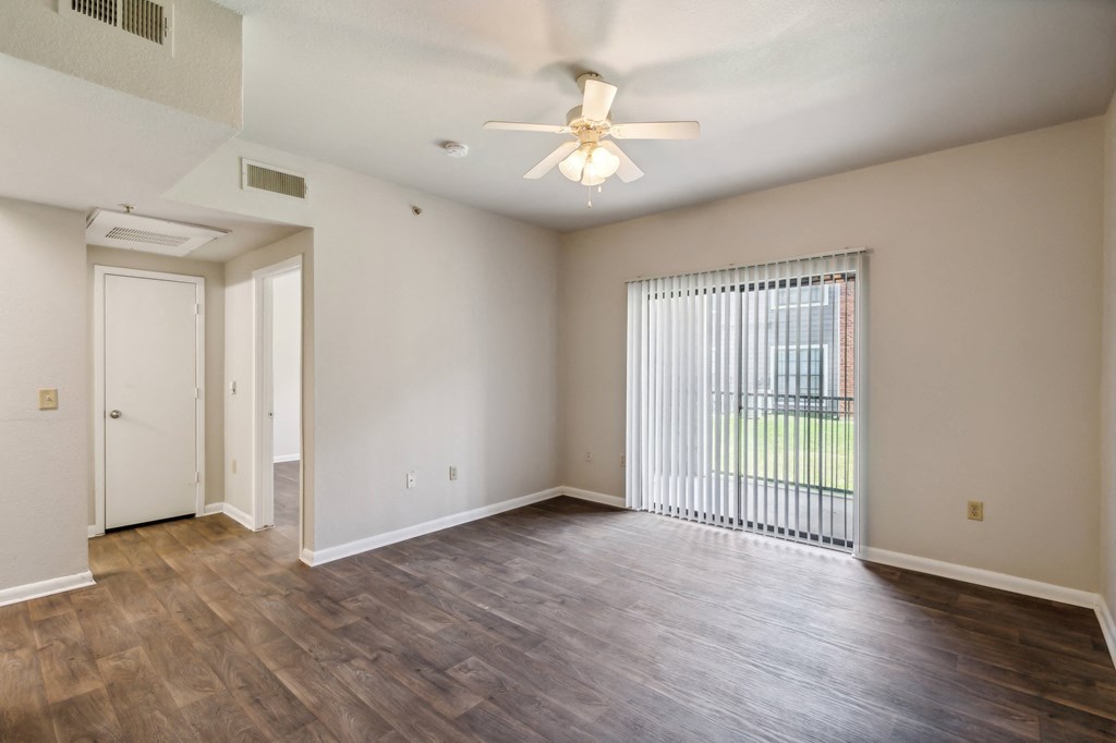 an empty living room with a large window and a ceiling fan