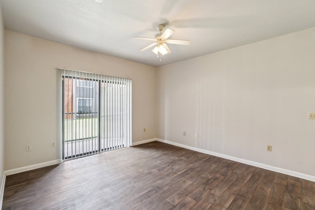 an empty living room with a large window and a ceiling fan