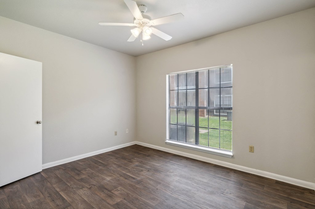 an empty living room with a large window and a ceiling fan