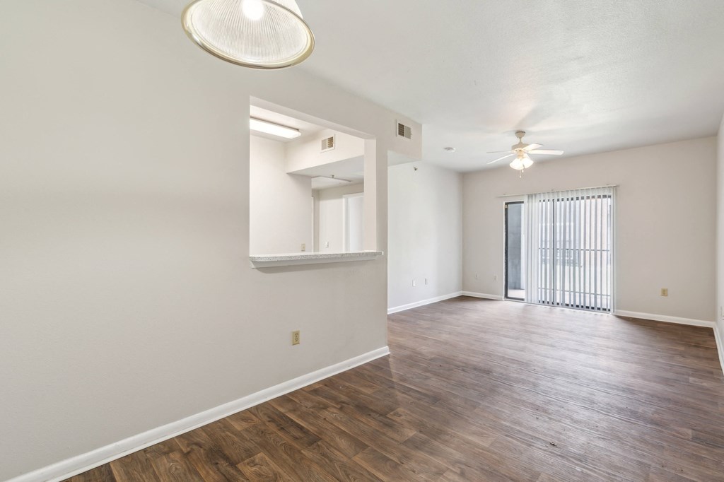 the living room and dining room of an apartment with wood floors and a ceiling fan