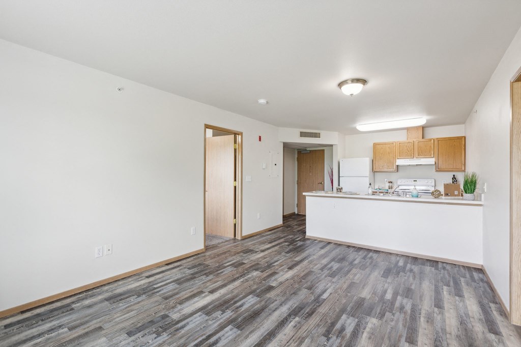 the living room and kitchen of an apartment with white walls and wood floors