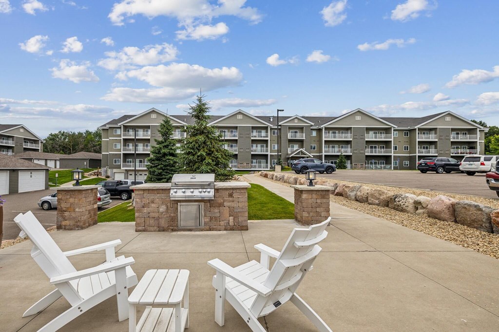 a patio with chairs and a grill in front of an apartment building a patio with chairs and a grill in front of an apartment building at Lake Ridge, Prior Lake, 55379