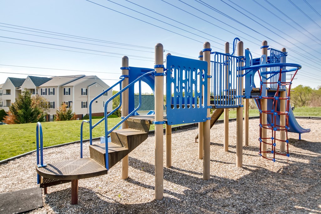 a playground with a blue playset and stairs in front of a building