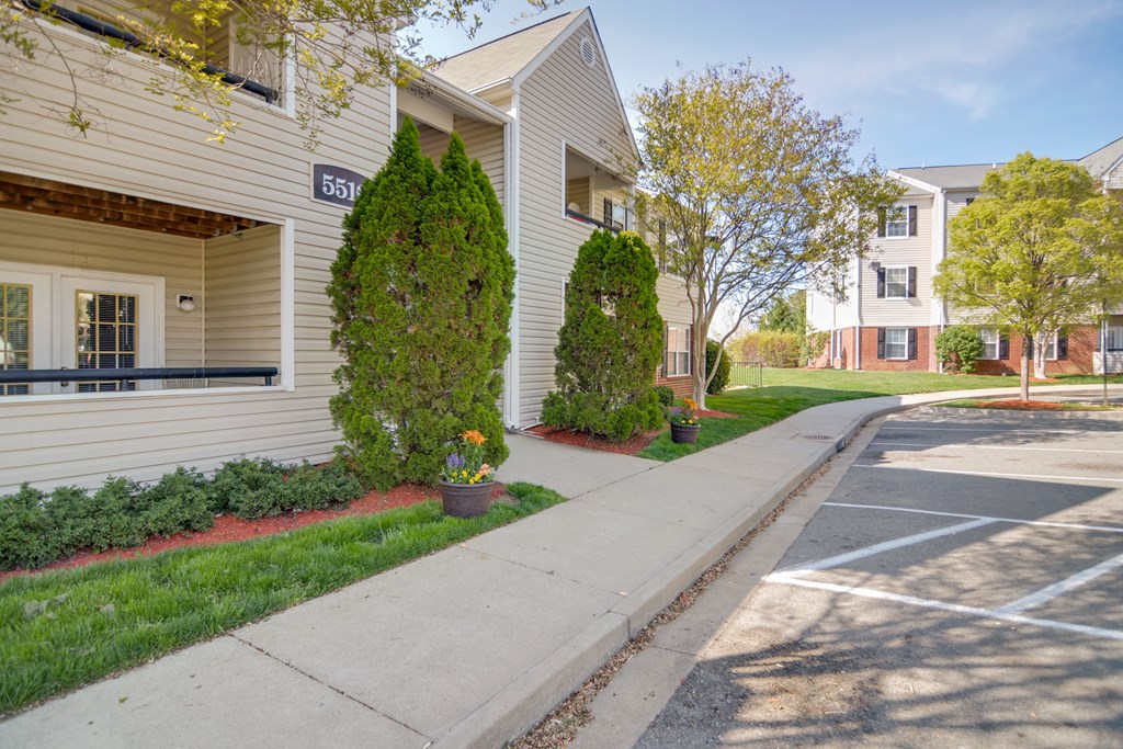 a sidewalk in front of a white apartment building with trees and grass
