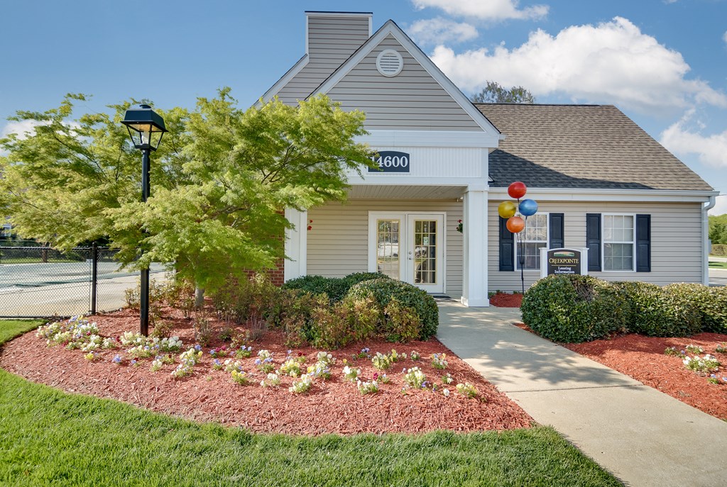 the front of a white house with a sidewalk and plants and a tree and balloons