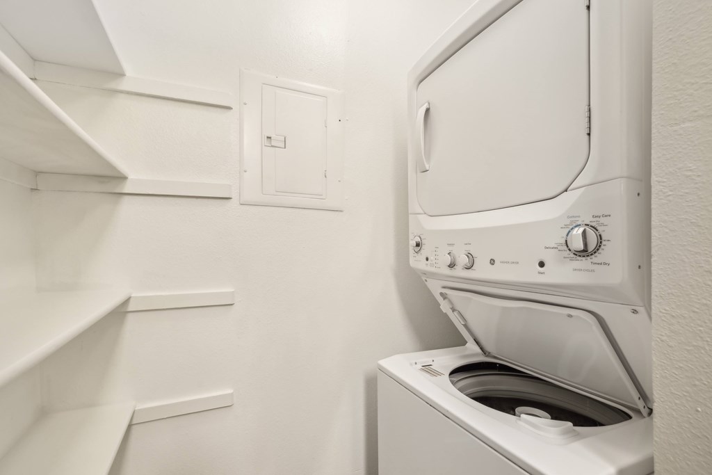 A white washing machine in a laundry room with shelves.
