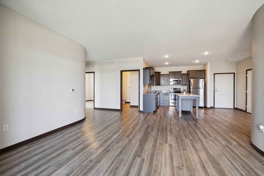 an empty living room and kitchen with wood floors and white walls