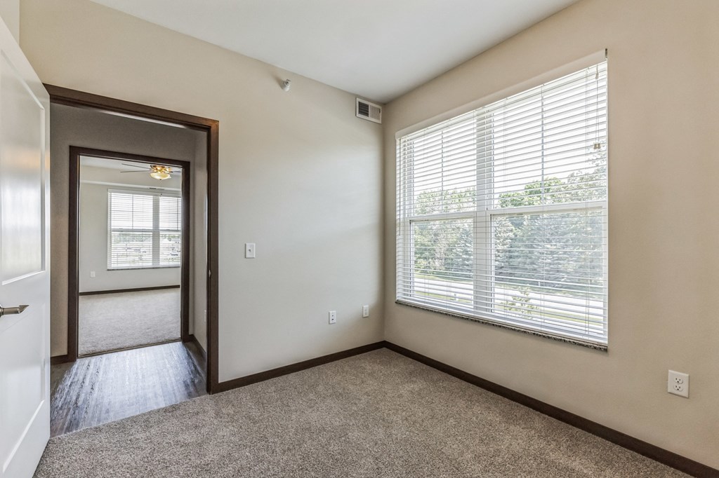 an empty living room with a large window and a door to a hallway