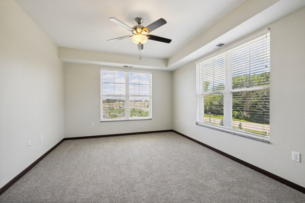 an empty living room with three windows and a ceiling fan