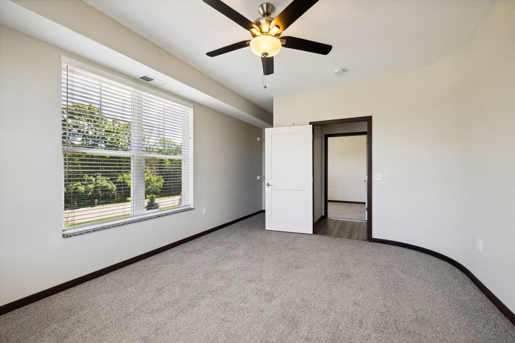 an empty living room with a large window and a ceiling fan