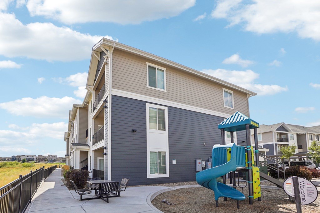 A playground area is in front of a two-story apartment building. at Connect at First Creek Apartments, Denver, CO