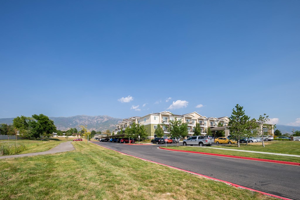 A road with cars parked on the side and apartment buildings in the background.