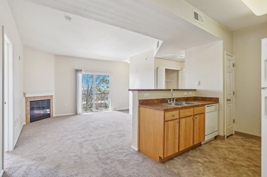 A spacious living room with a fireplace and a kitchen area with wooden cabinets and white appliances. at Stetson Meadows Apartments, Colorado Springs